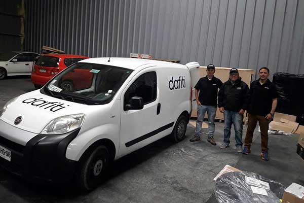 tres personas del equipo de kwt courier posando al lado de un furgon de carga blanco